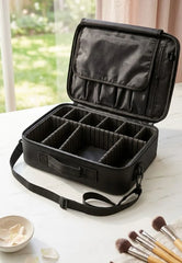 Black travel makeup case with compartments on a white surface with brushes and a bowl.